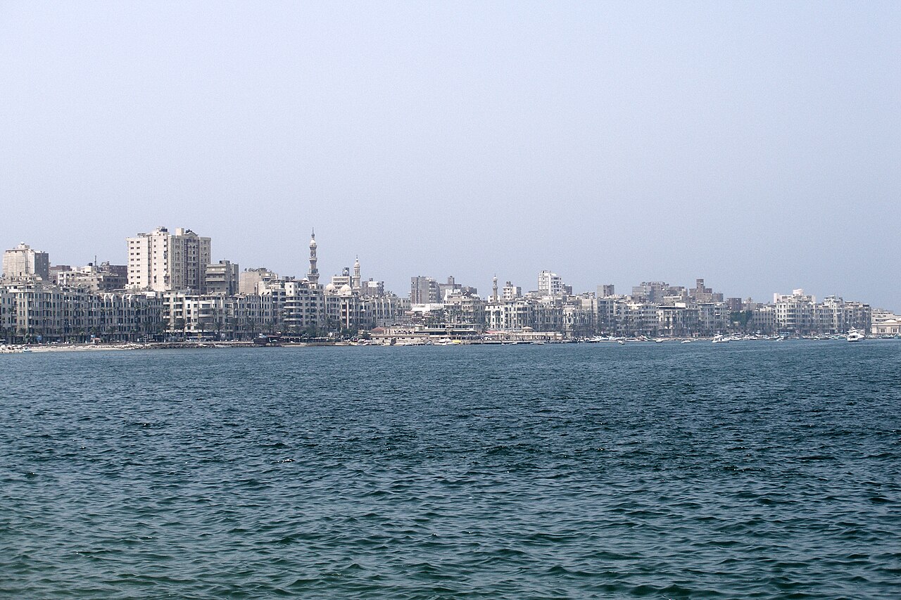 Mediterranean Sea waves crashing on Alexandria rocky coastline with fishing boats in distance