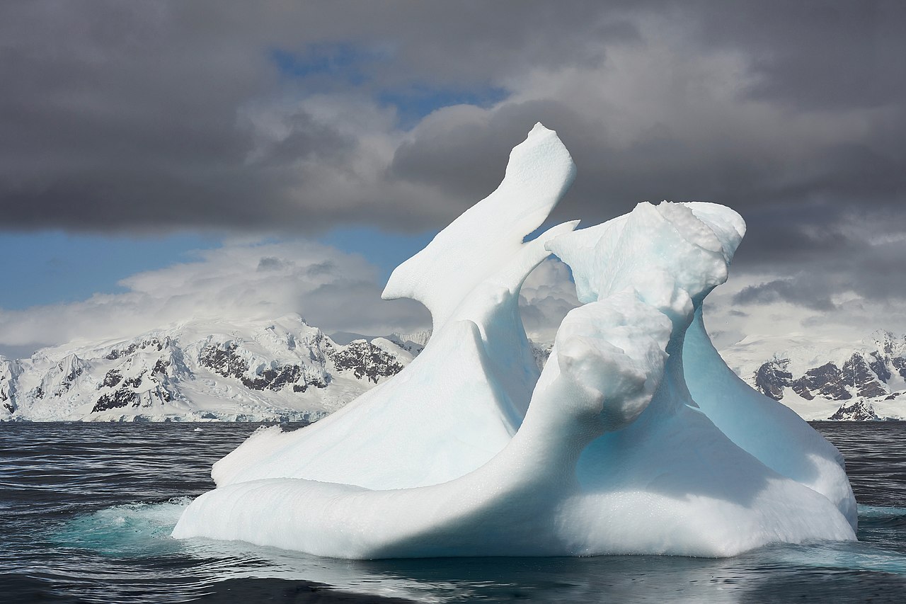 Massive blue iceberg floating in Antarctic waters with intricate carved shapes from erosion