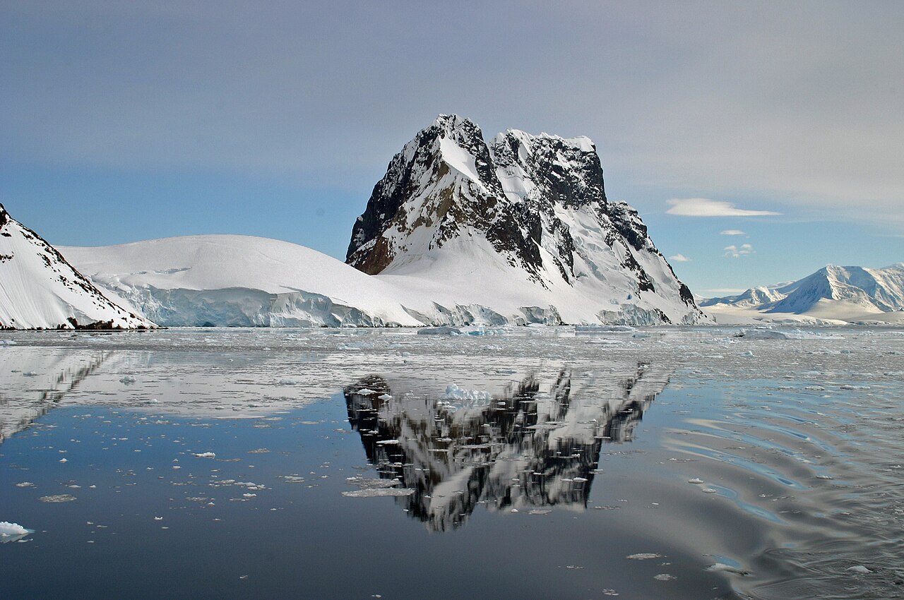Expedition ship navigating through narrow Lemaire Channel between towering ice cliffs