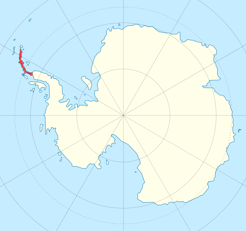 Massive glacier wall meeting dark blue Antarctic waters with scattered icebergs and mountain peaks in background