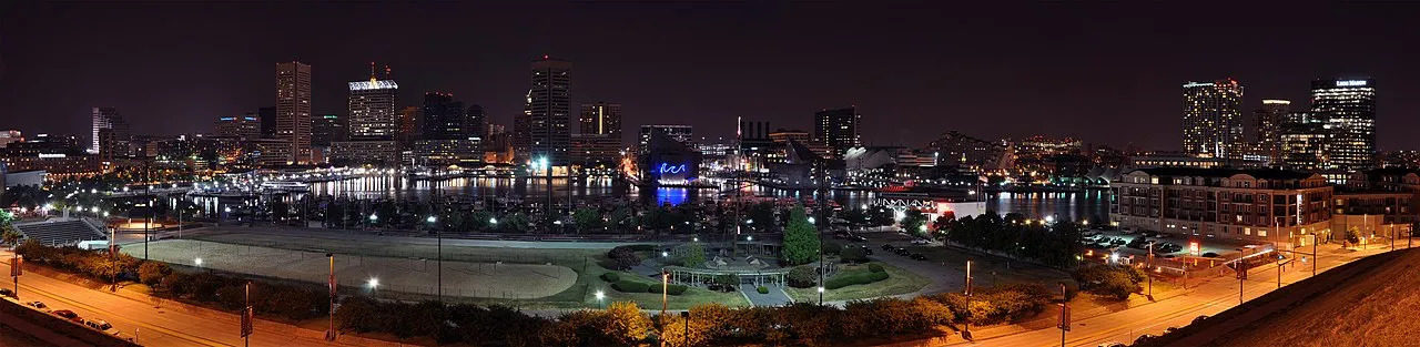 Nighttime panorama of Baltimore Inner Harbor skyline with city lights reflected in water