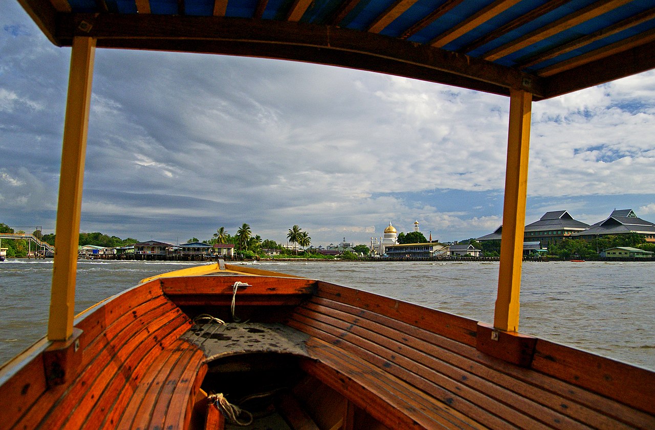 View from a wooden water taxi on the Brunei River approaching Kampong Ayer, with Omar Ali Saifuddien Mosque dome visible
