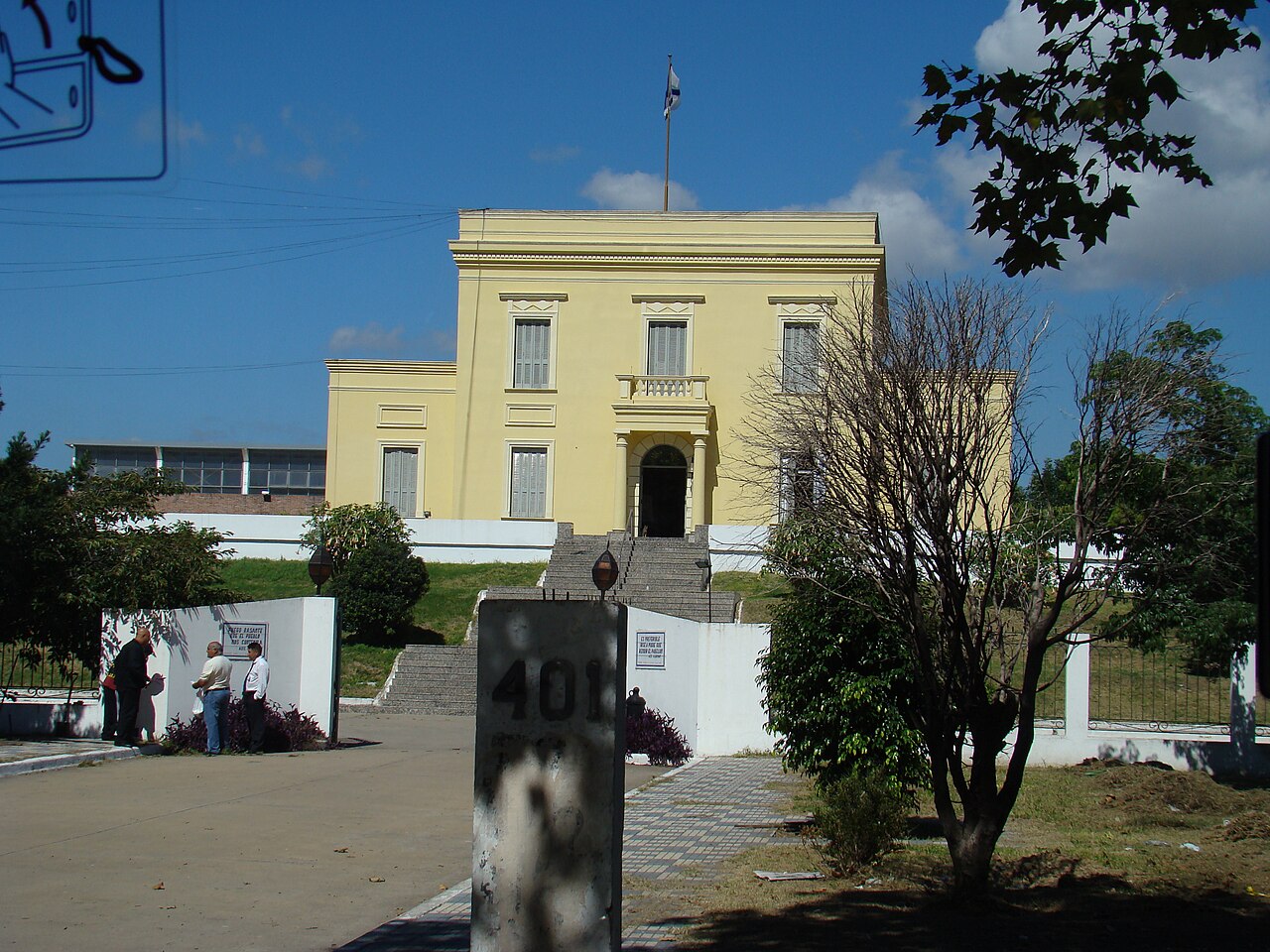 Yellow neoclassical building with Argentine flag flying, stone staircase, in a Buenos Aires park