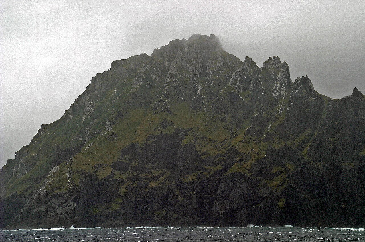 The dark jagged peak of Cape Horn island rising from rough grey seas with clouds wrapping the summit