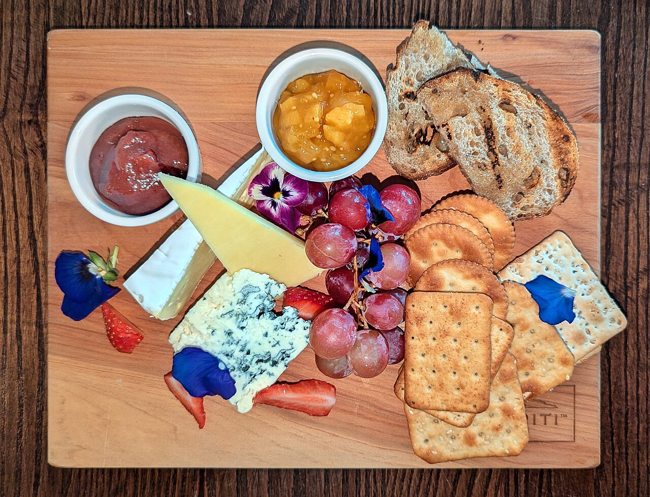 Artisanal New Zealand cheese board with blue cheese, brie, grapes, crackers, and edible flowers