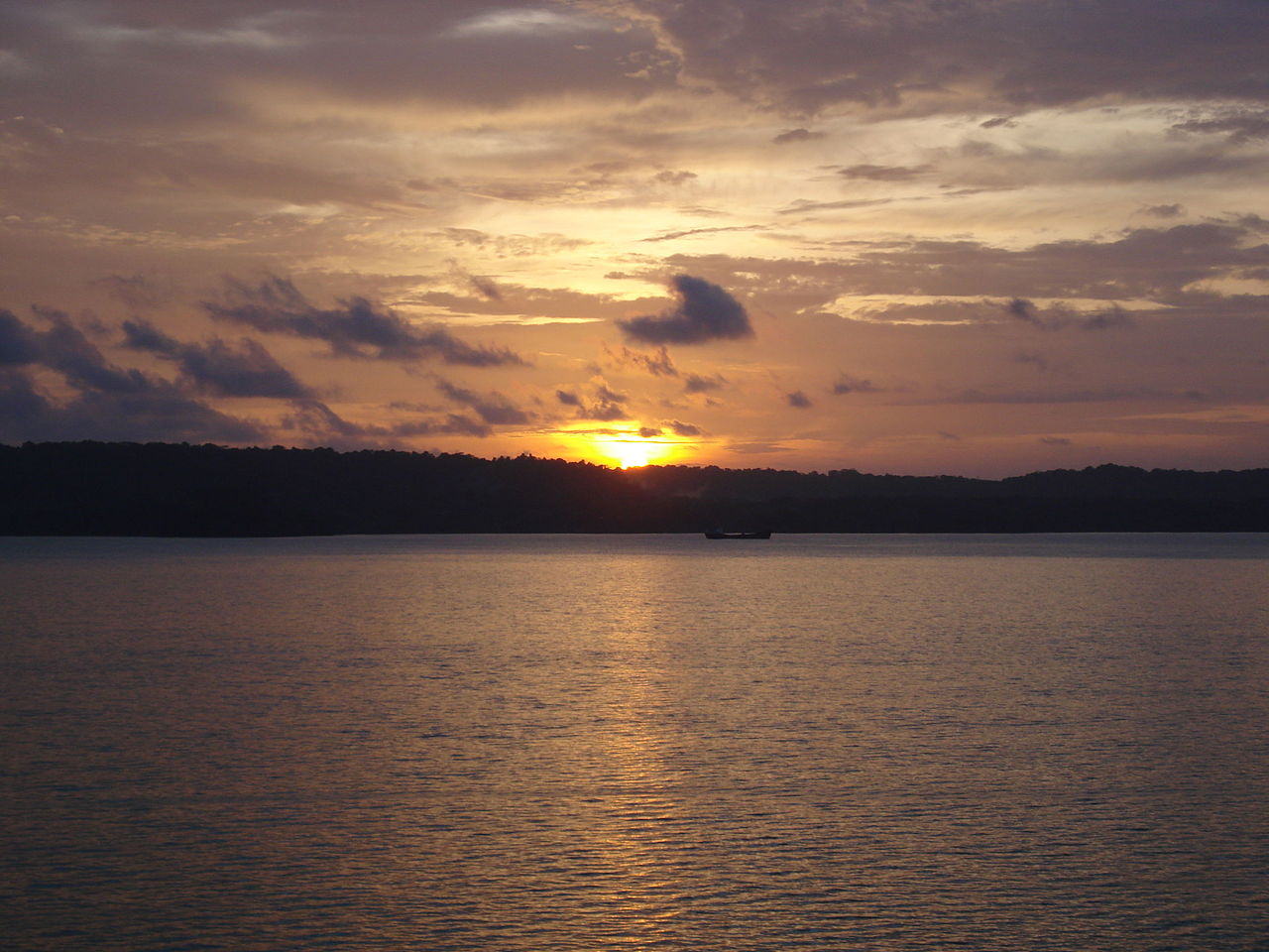 Sunset over the calm tropical waters near the Panama Canal with jungle-covered hills silhouetted