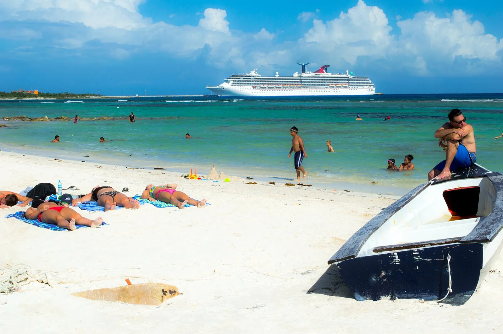 Mahahual beach with Carnival cruise ship in background, beachgoers, and fishing boat in foreground