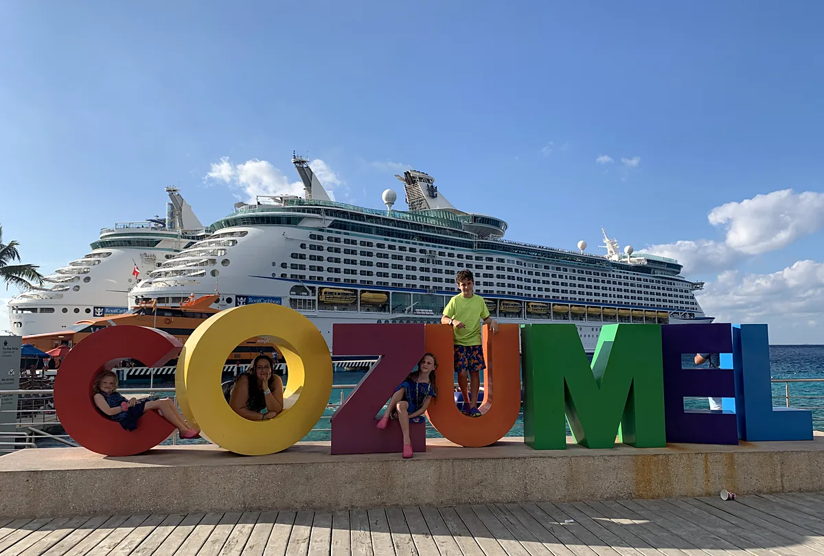 Family at the colorful COZUMEL sign with Royal Caribbean ship docked behind