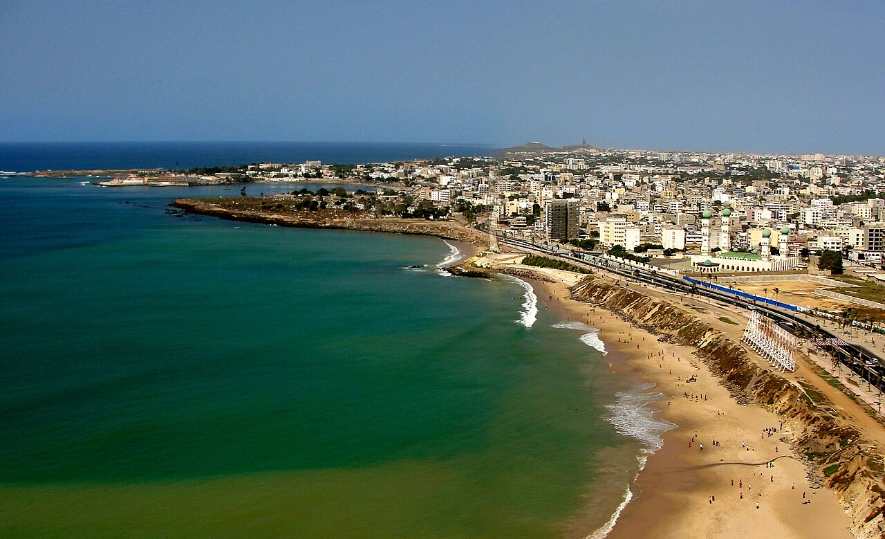 Aerial view of Dakar coastline with beaches, train, and African Renaissance Monument in distance