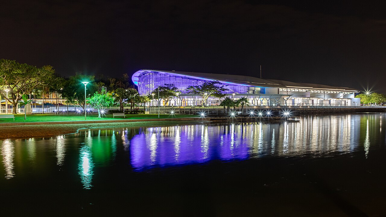 Darwin Convention Centre illuminated in purple at night, reflected in the waterfront lagoon