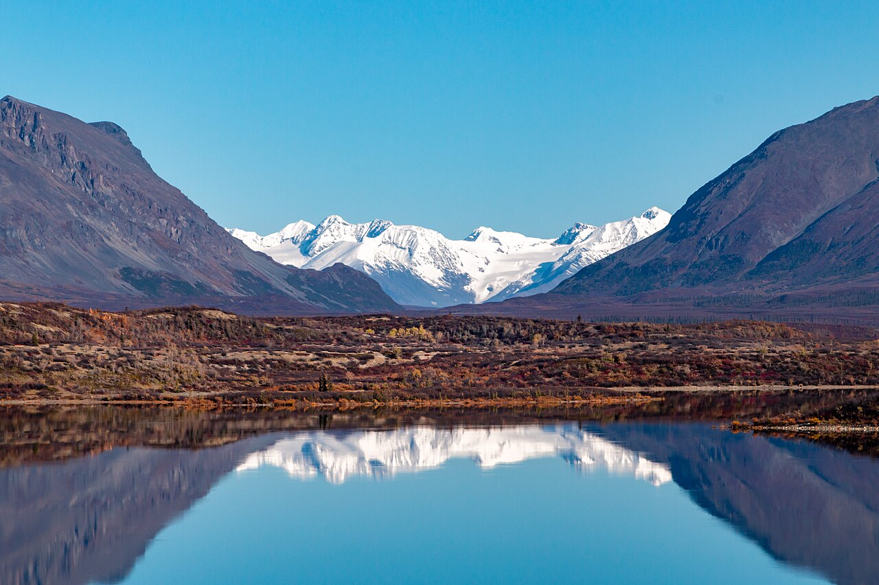Snow-capped Alaska Range peaks perfectly reflected in still alpine lake with autumn tundra, Denali National Park