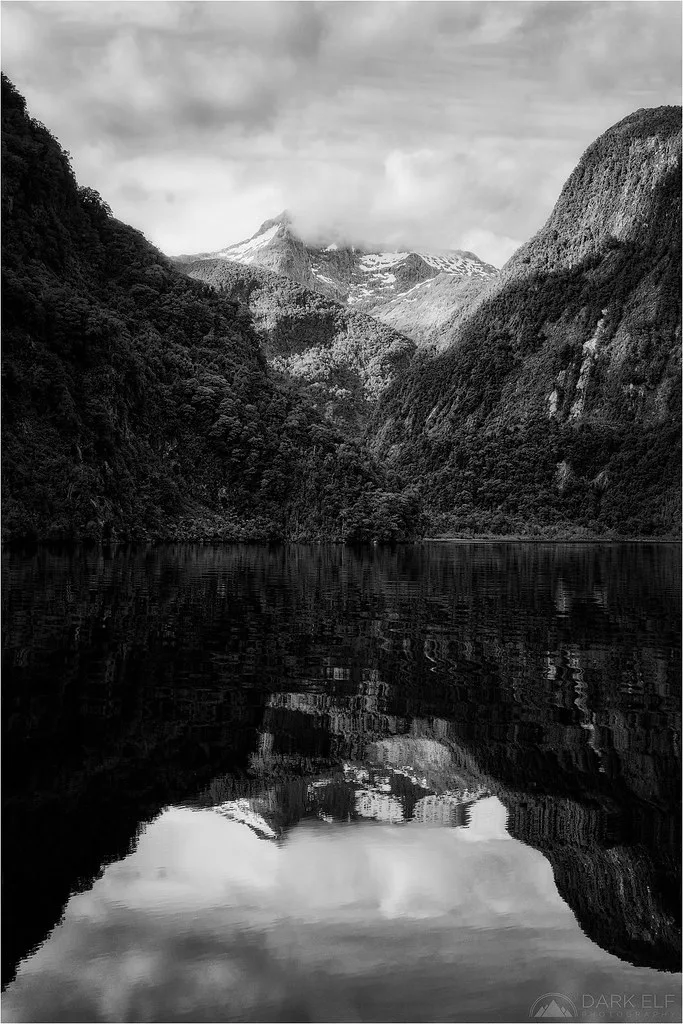 Waterfalls cascading down sheer granite cliffs into the dark waters of Doubtful Sound
