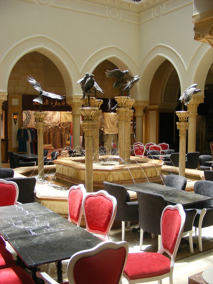 Ornate Arabic courtyard restaurant with falcon sculptures on fountain columns and red velvet chairs