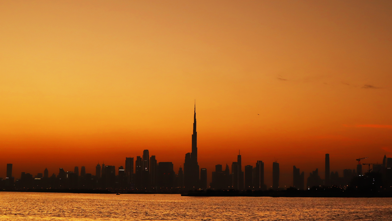 Silhouette of Dubai skyline with Burj Khalifa against a vivid orange sunset over the Arabian Gulf