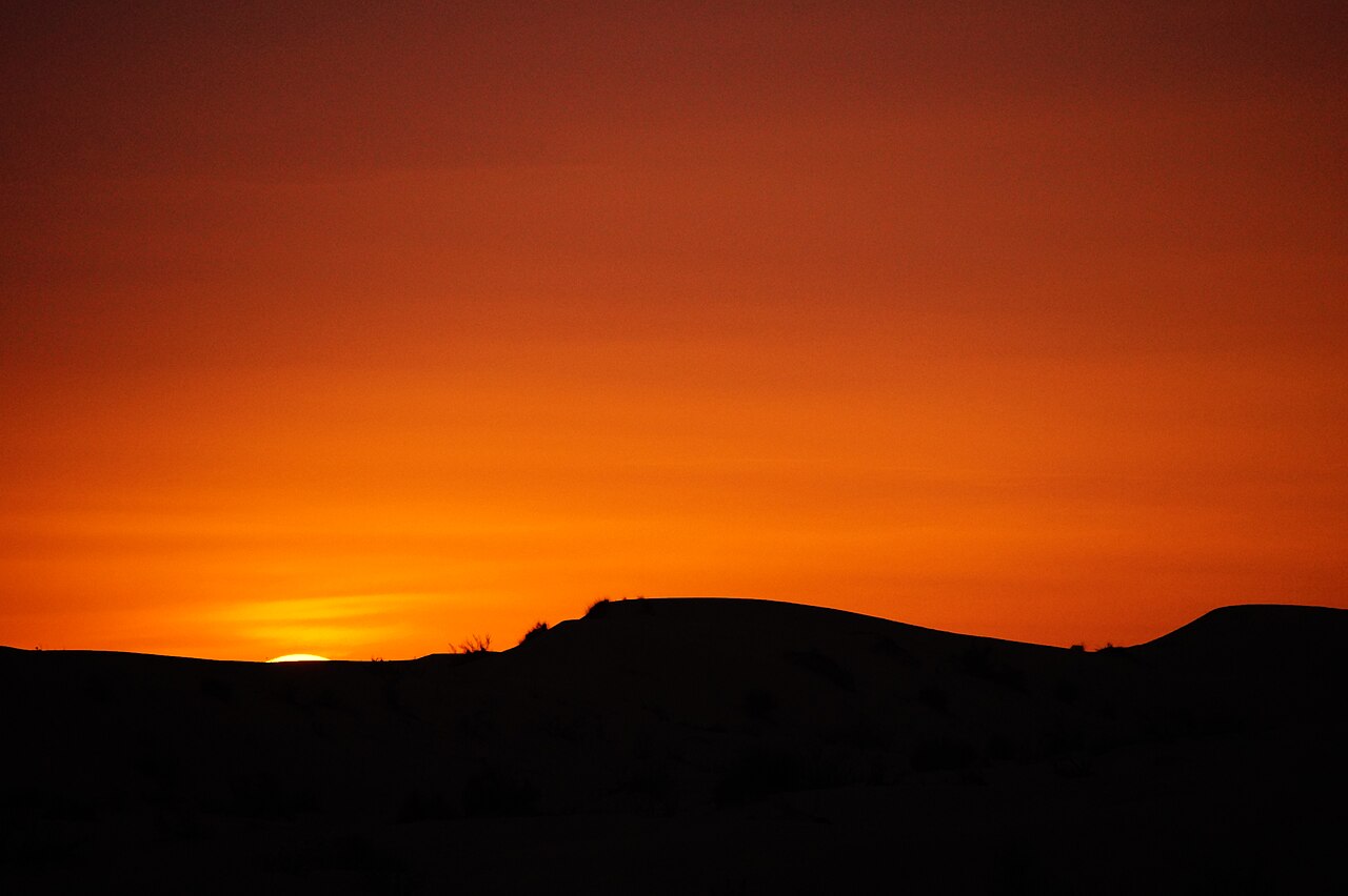 Sunset over Arabian desert sand dunes with the sun touching the silhouetted dune ridgeline