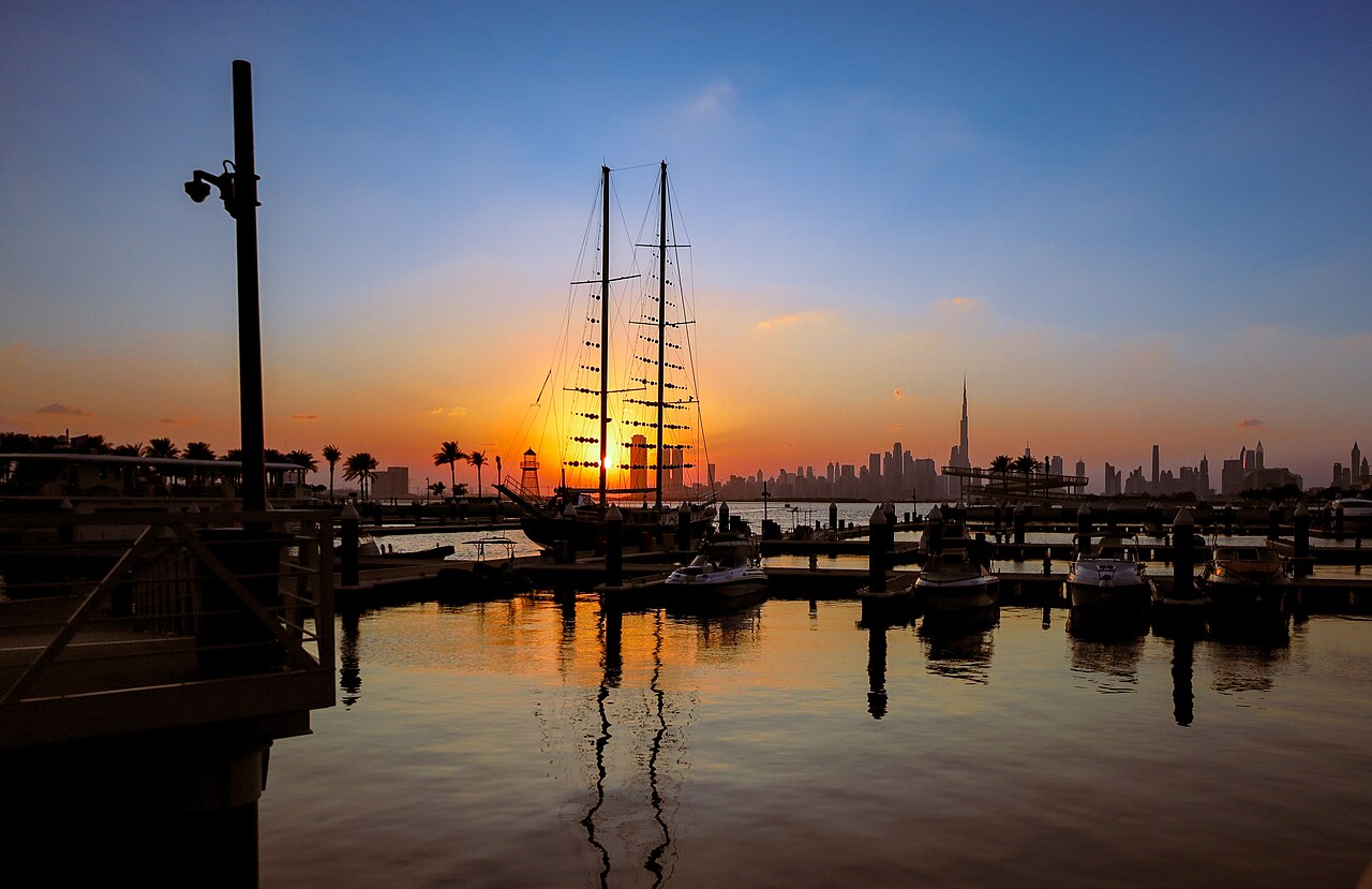 Sunset silhouette of a marina with sailboat masts and the Dubai skyline including Burj Khalifa in the background