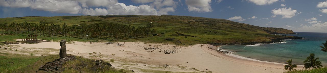 Panoramic view of Anakena Beach on Easter Island with white sand, palm trees, moai at Ahu Nau Nau, and green volcanic hills
