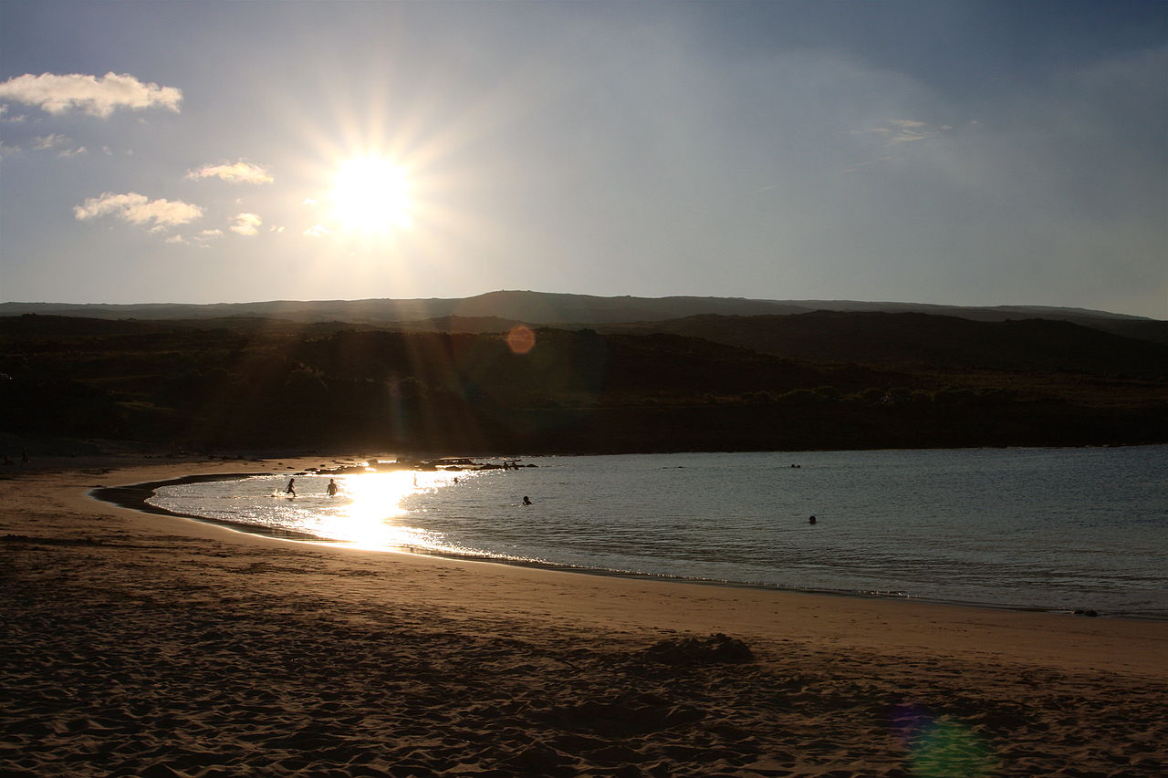 Sunset over a crescent beach on Easter Island with volcanic hills silhouetted and swimmers in the water