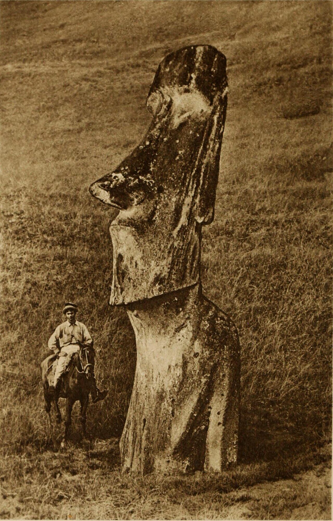 Historical sepia photograph of a man on horseback dwarfed by a towering moai statue on Easter Island