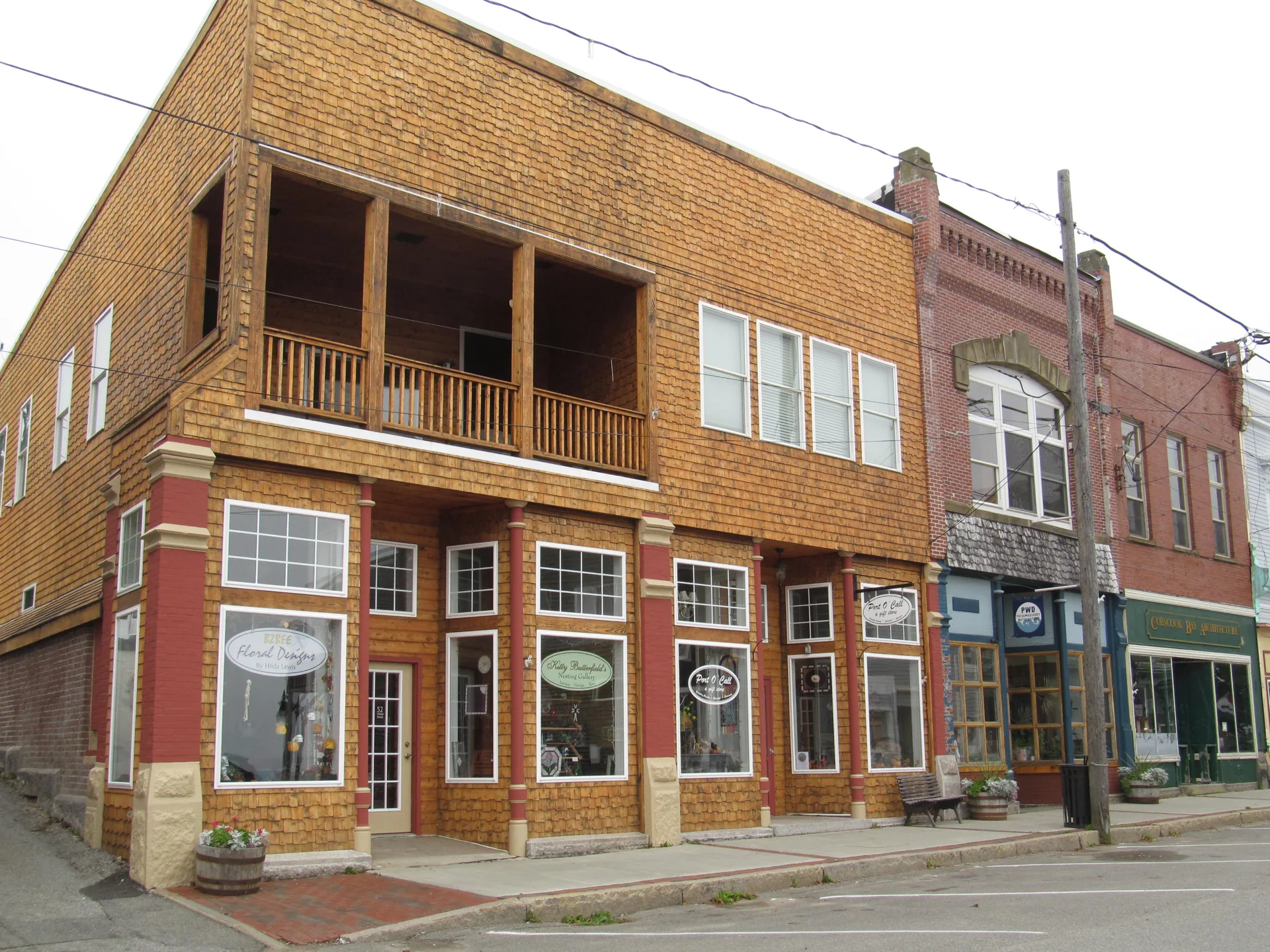 A row of shingled and brick shopfronts along Water Street in Eastport, with a floral shop, a corner store, and small businesses under a grey sky
