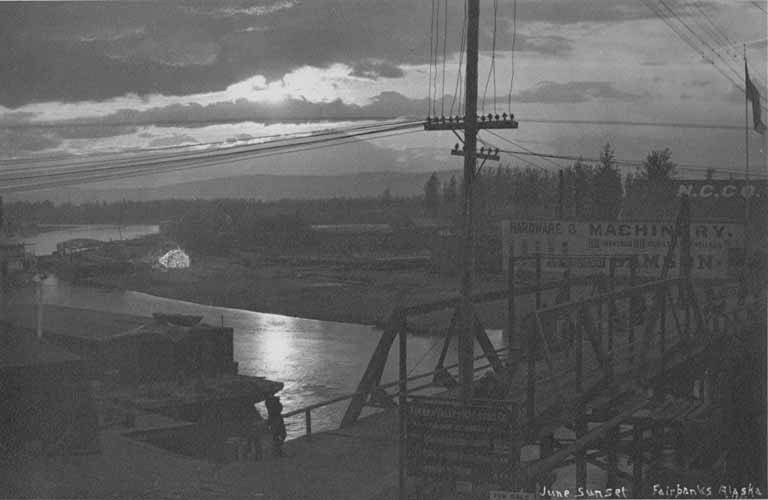 June sunset over Fairbanks with Tanana Valley Railroad Company sign in foreground, circa 1907-1913