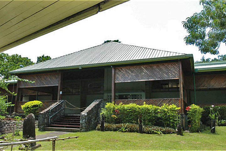 Traditional Fijian bure building with corrugated roof, lattice walls, stone base, and tropical garden