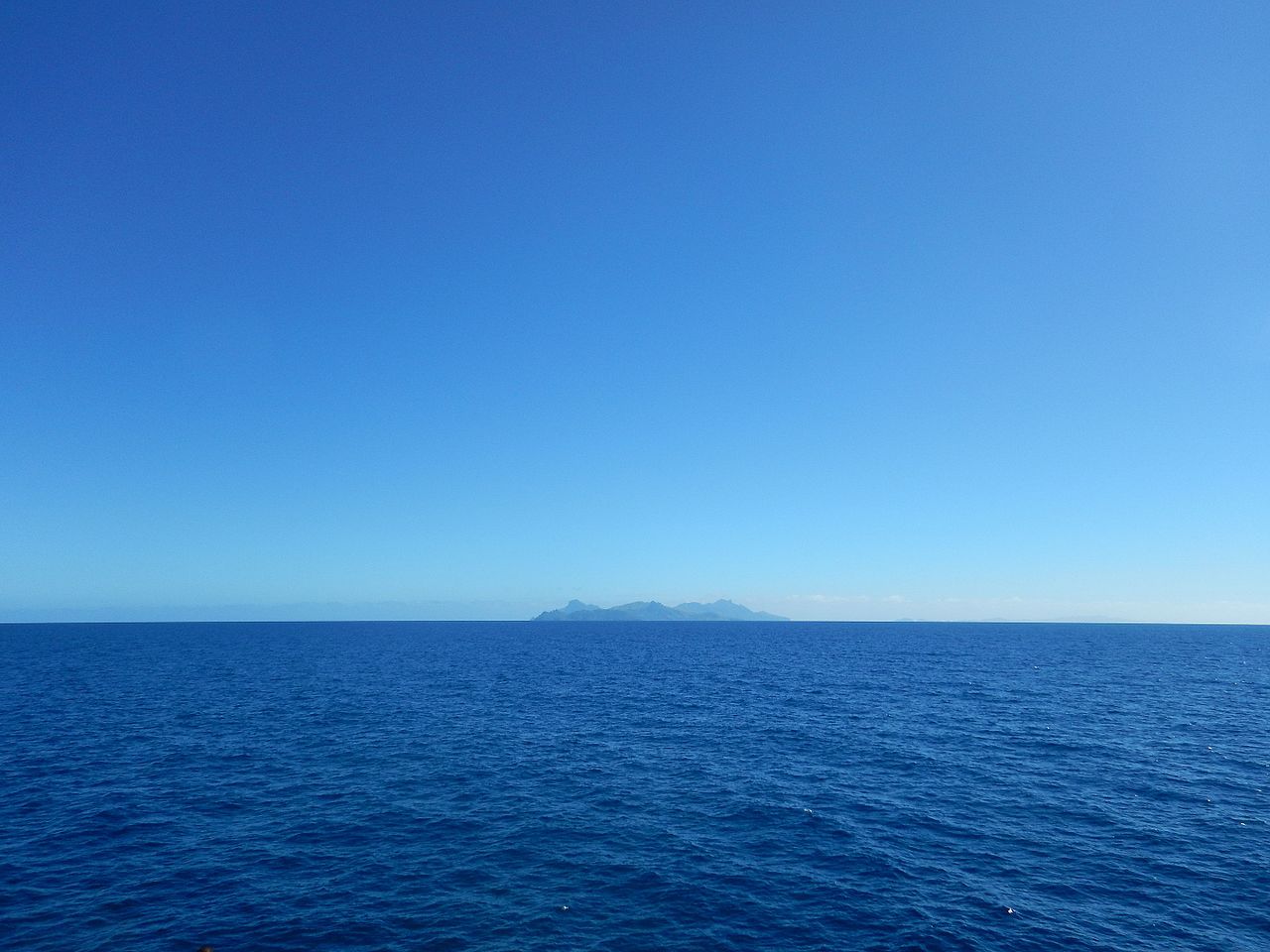 Distant Fijian island with volcanic peaks on the horizon seen from a ship crossing deep blue Pacific waters