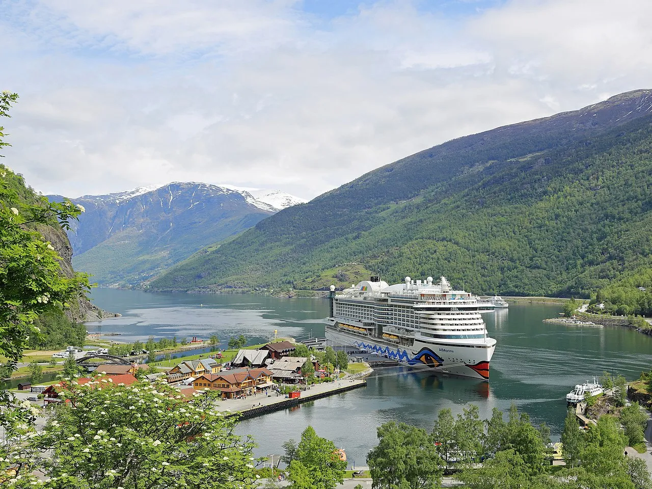 The Flamsbana railway train winding through a steep green valley with waterfalls cascading down granite mountainsides