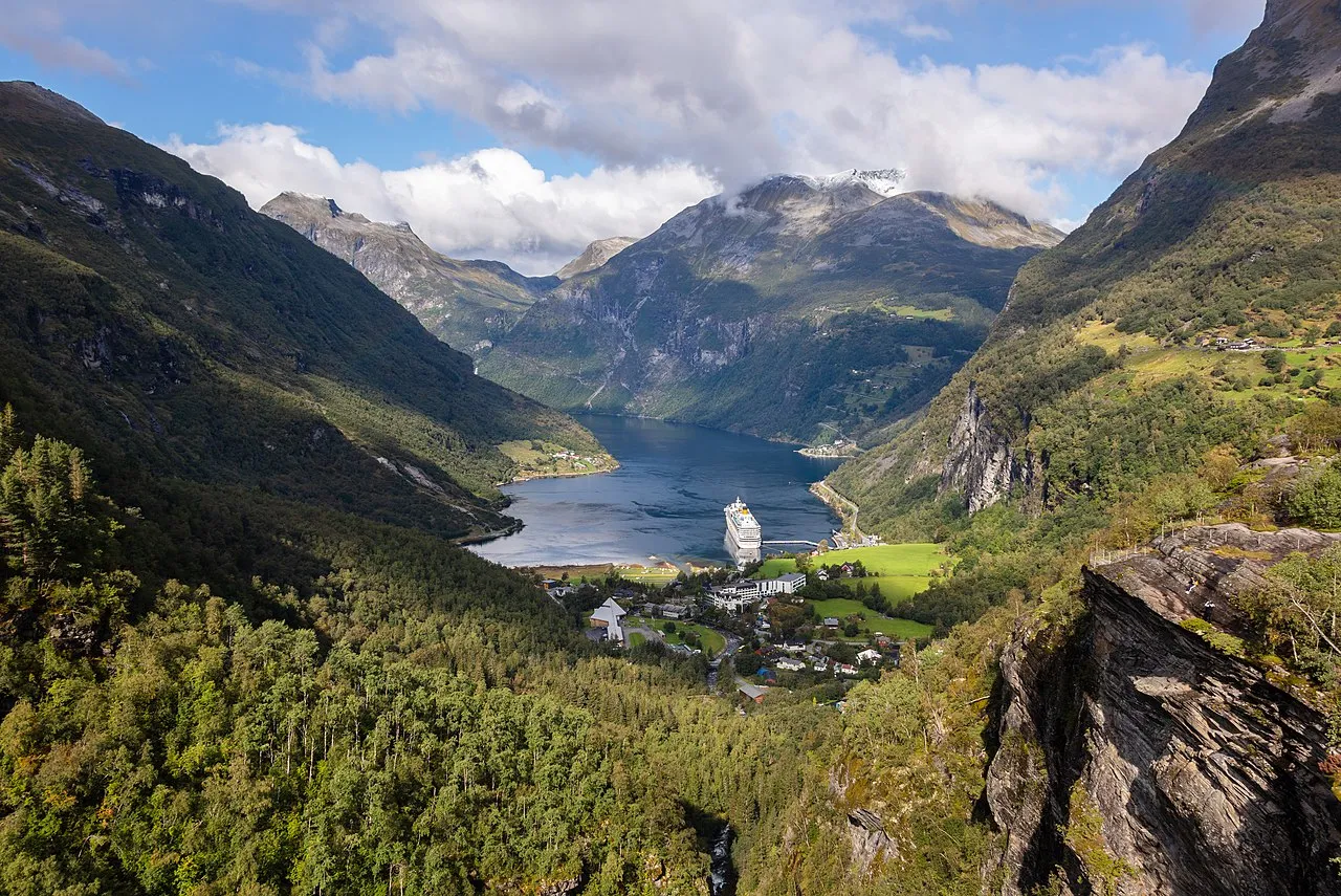 Seven Sisters waterfall cascading down sheer cliff face into the emerald waters of Geirangerfjord with mist rising from the spray