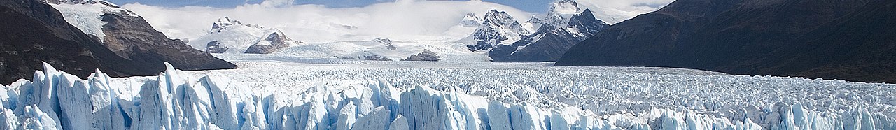 Panoramic view of Patagonian glacier with jagged ice formations and snow-capped mountains