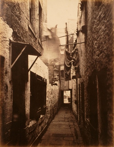 Historical sepia photograph of a narrow Glasgow close with laundry hanging between tenement walls, circa 1870s