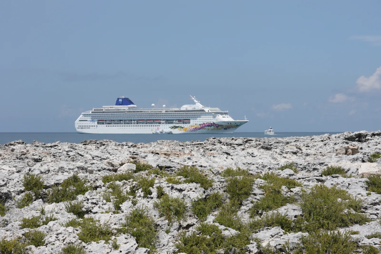 Norwegian Sky anchored beyond the rugged limestone-and-scrub shoreline of the cay with a small boat alongside