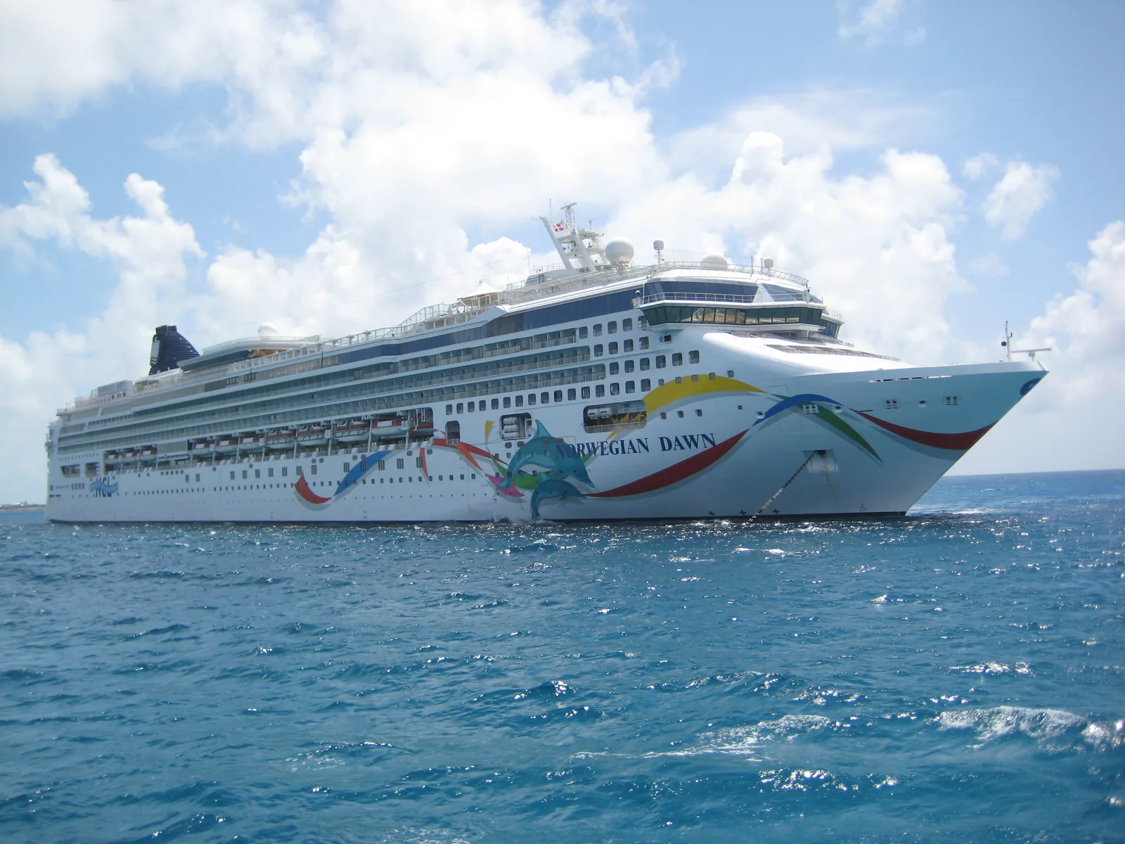 NCL's Norwegian Dawn anchored off the cay, white hull with a colourful abstract bow livery on deep blue water
