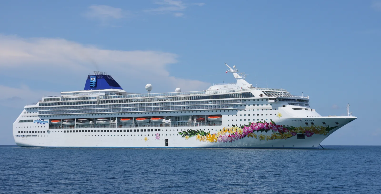 Norwegian Sky anchored off the cay, white hull with NCL funnel mark and hibiscus bow livery