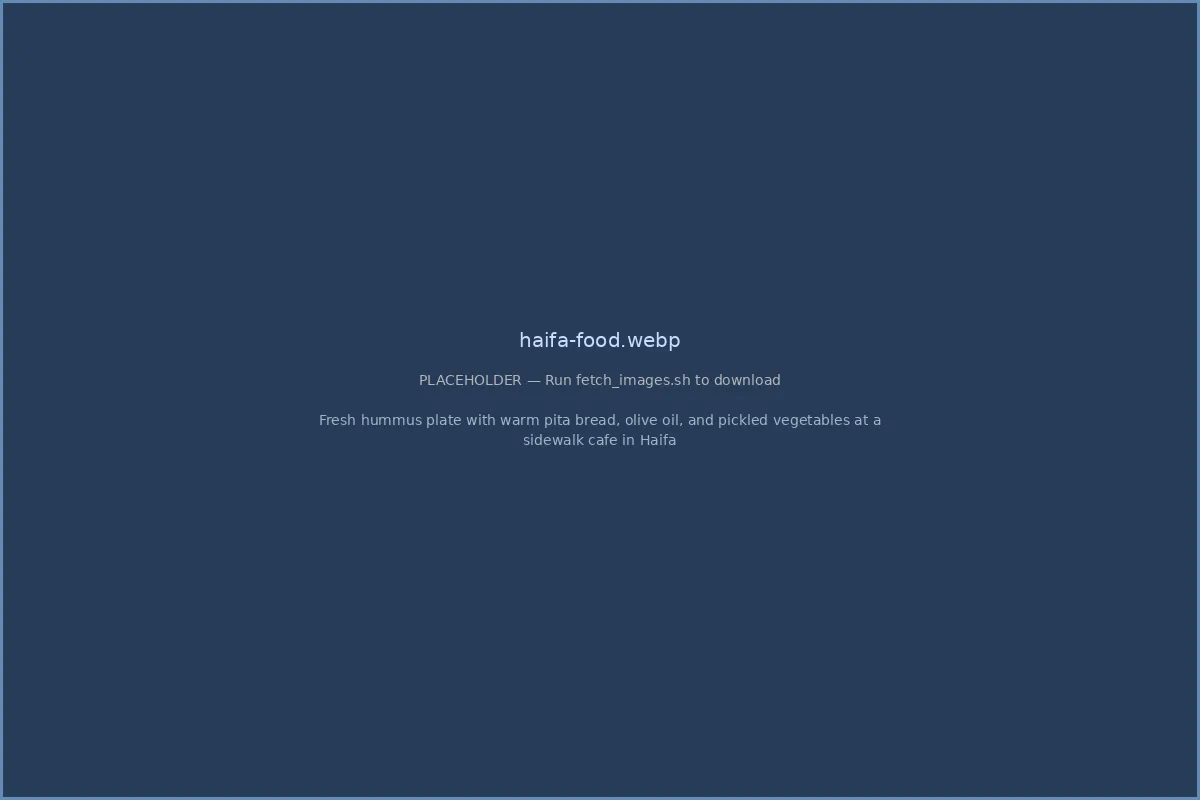 Fresh hummus plate with warm pita bread, olive oil, and pickled vegetables at a sidewalk cafe in Haifa