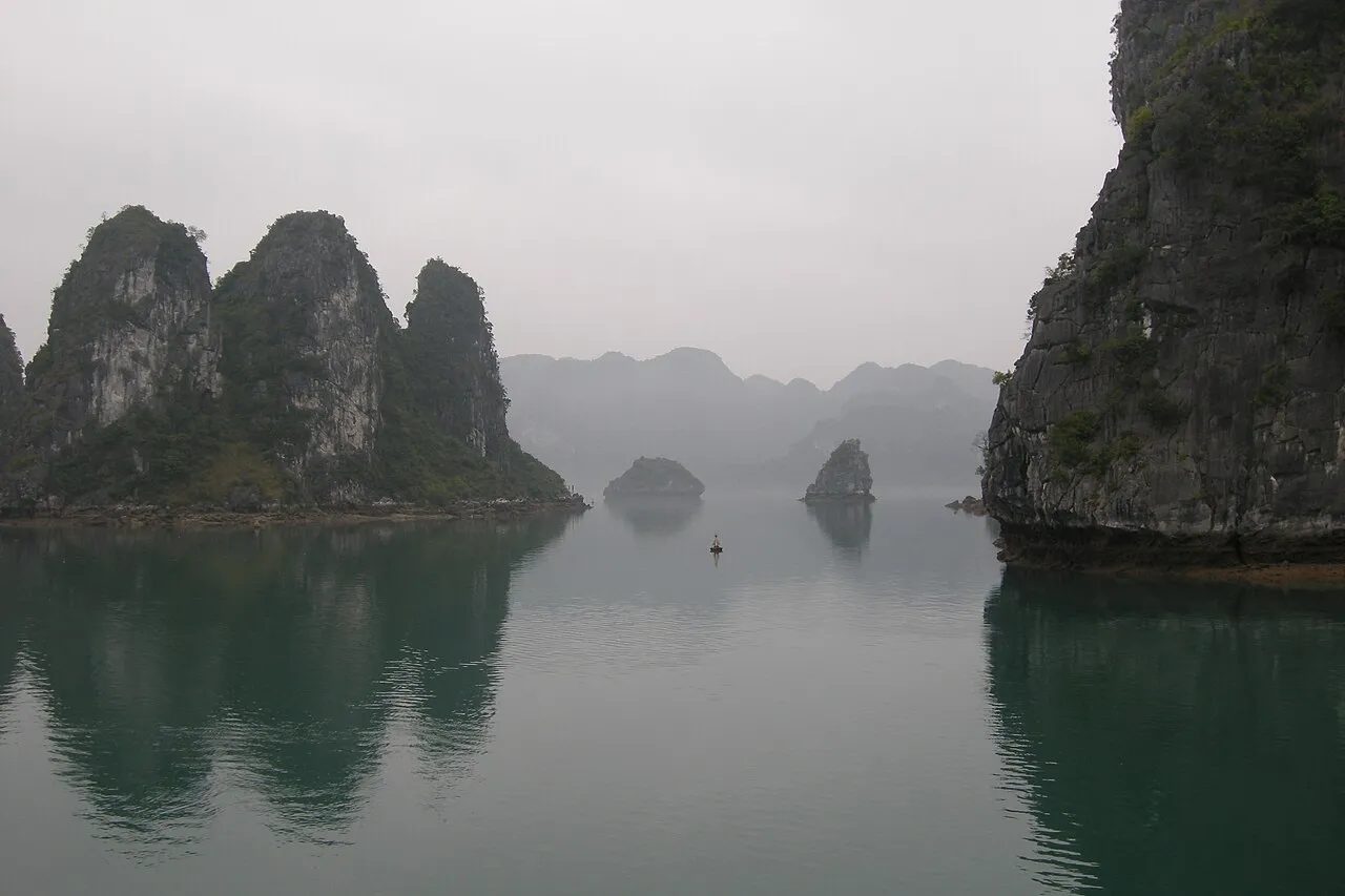 Misty karst limestone pillars reflected in emerald water with lone boat