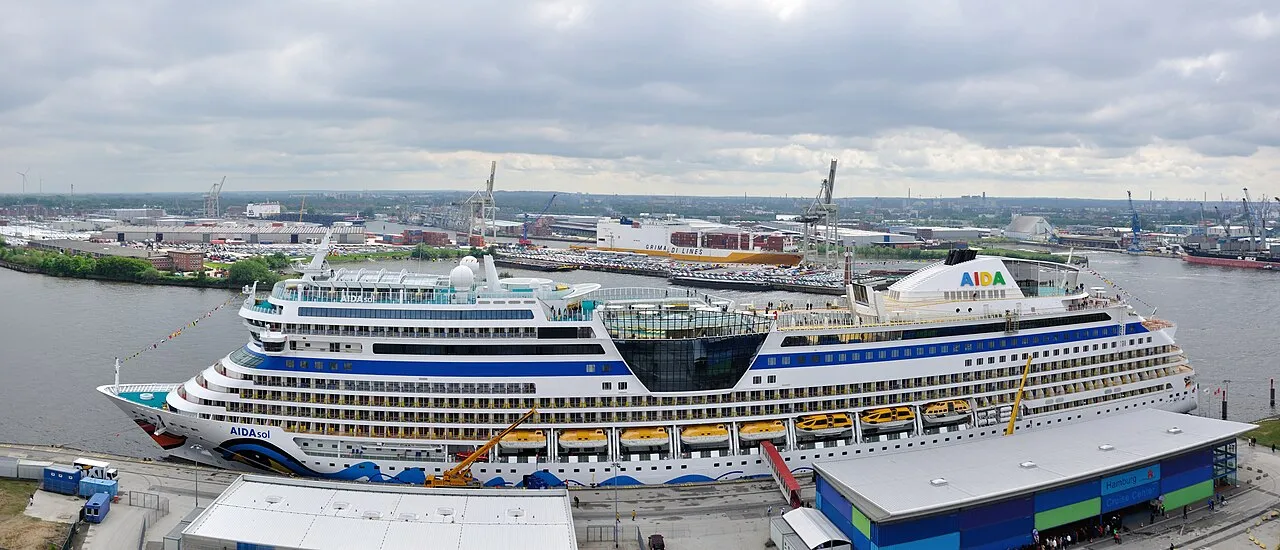 AIDAsol cruise ship docked at Hamburg Cruise Center with industrial port cranes and container ships in the background