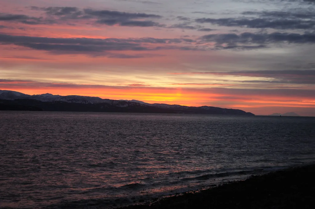 Sun setting over purple and orange mountains across Kachemak Bay from Homer Spit