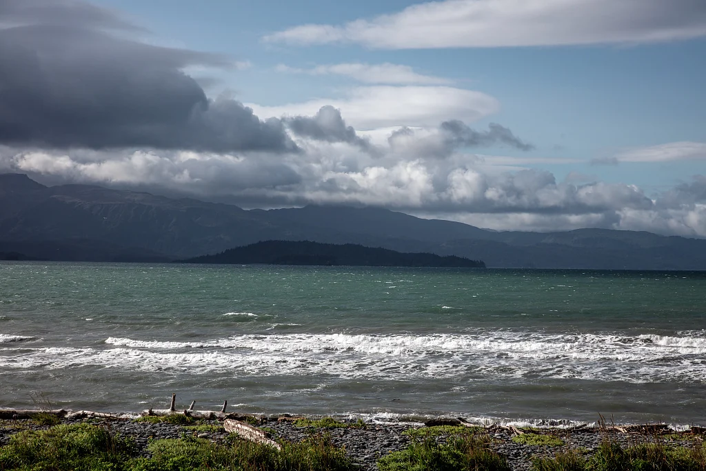 Windy afternoon with waves breaking on a Homer gravel beach and the Kenai Mountains across Kachemak Bay