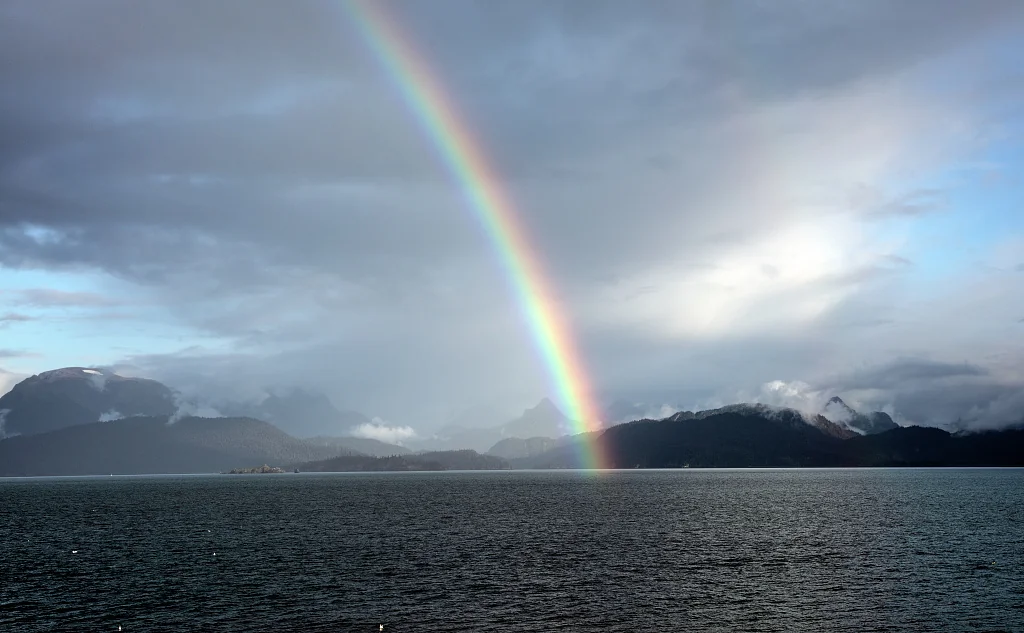 Vivid rainbow arching over Kachemak Bay from Homer, touching the Kenai Mountain shoreline