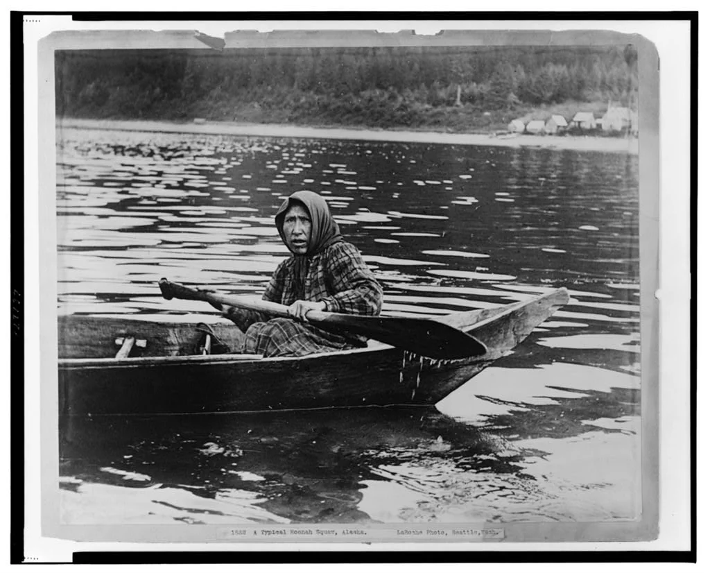 1903 sepia photograph of a Huna Tlingit woman in a traditional dugout canoe with a paddle near Hoonah