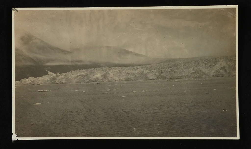 Circa-1910 sepia photograph of the Muir Glacier face across calm water