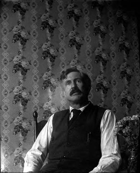 Historic photograph of a man seated in front of floral wallpaper, Inland Passage, circa 1906