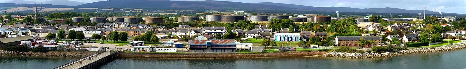 Panoramic view of Invergordon from Cromarty Firth showing pier, town, and oil storage tanks with Highland hills