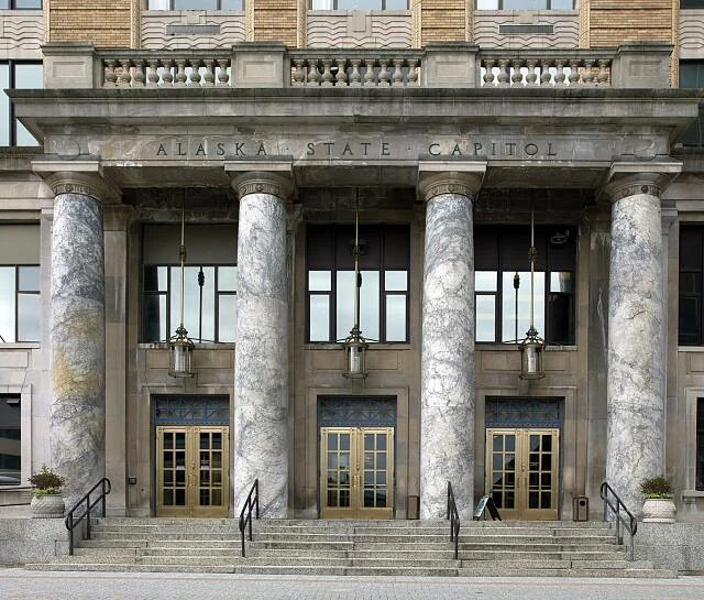 Front entrance of the Alaska State Capitol building with four marble columns and carved inscription
