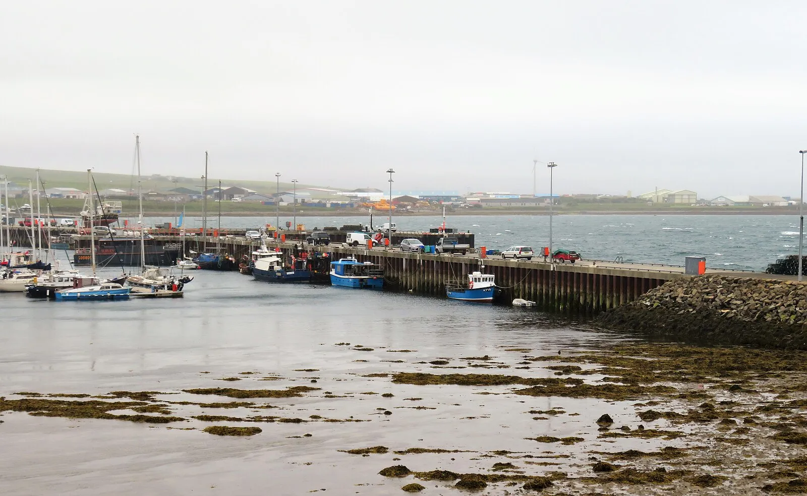 Kirkwall harbor pier at low tide with fishing boats and green fields