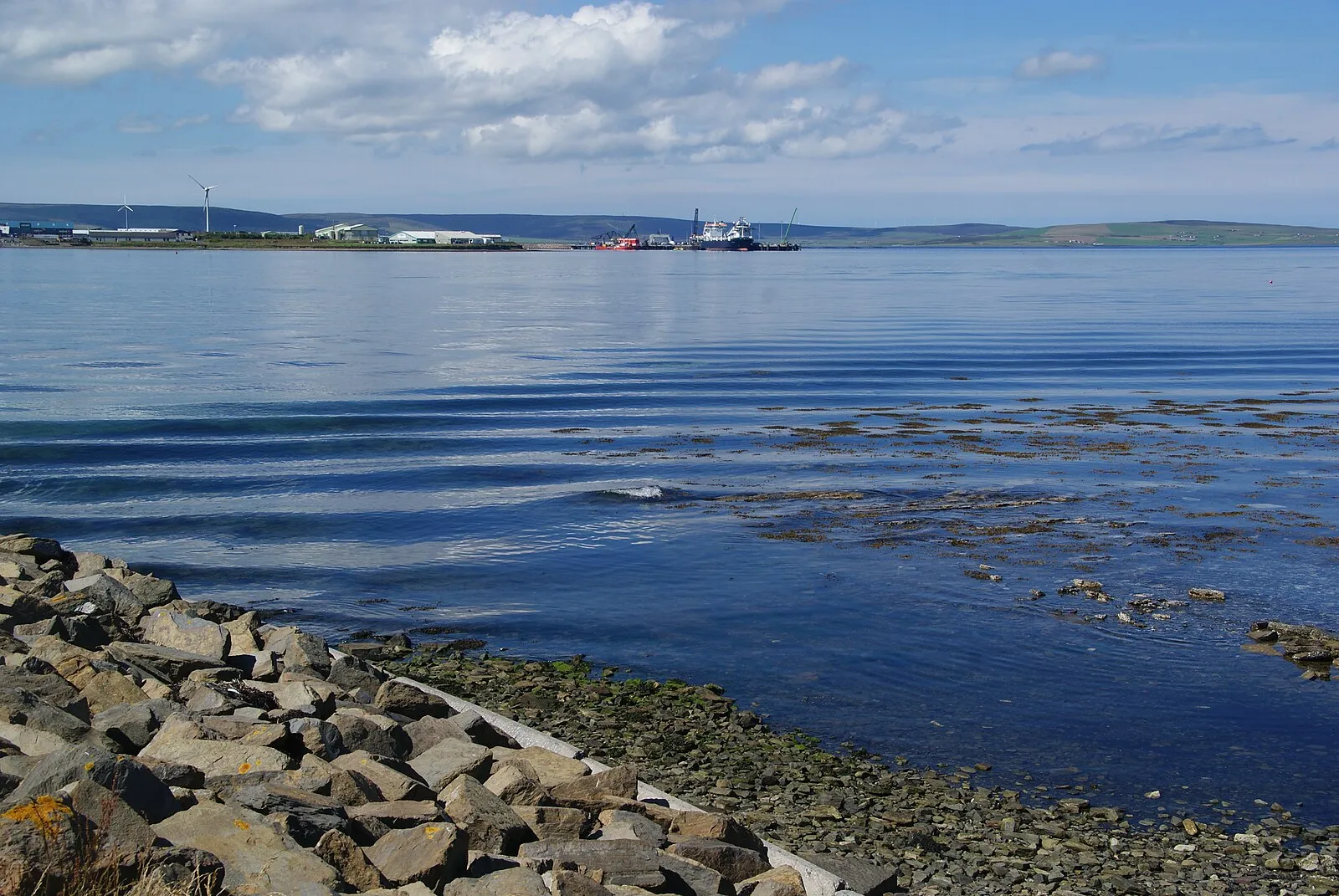 Calm Kirkwall Bay with wind turbine, port facilities and blue sky