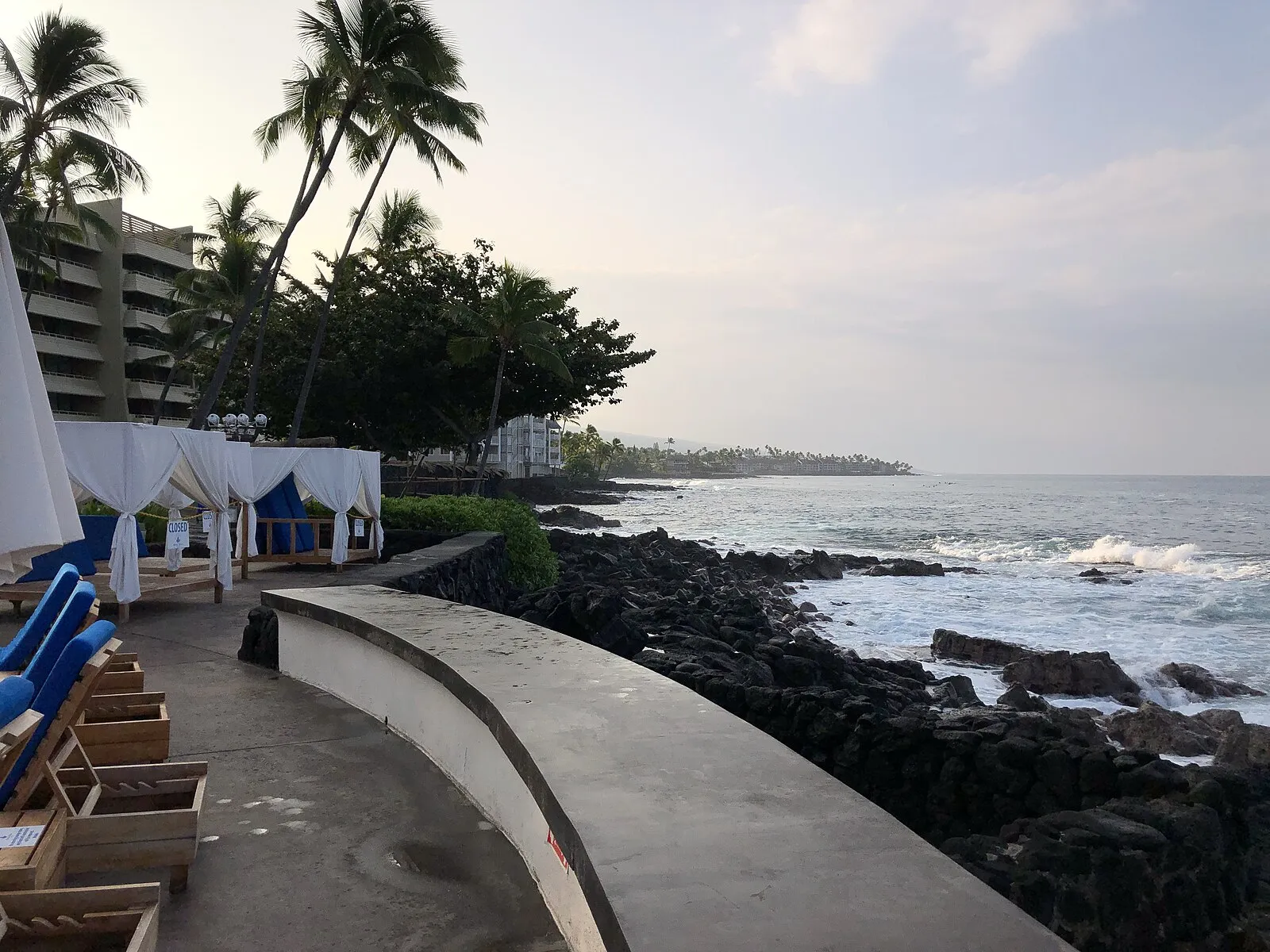 Kona resort oceanfront with cabanas, palms, and black lava rock coast