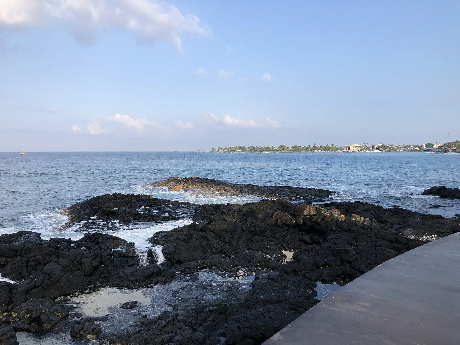 Black lava rock shoreline with Kailua Bay and town across the water