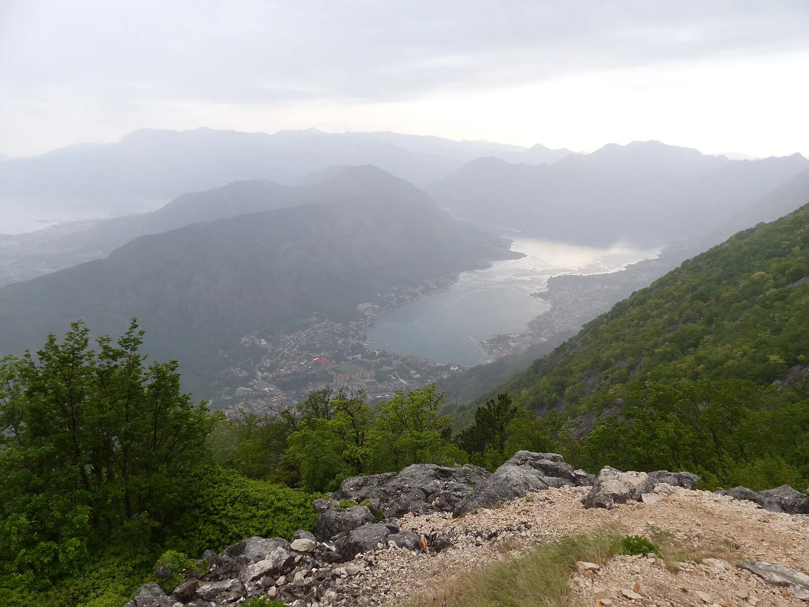 Aerial view of Kotor cruise port with a large ship docked alongside the medieval walled Old Town and surrounding mountains